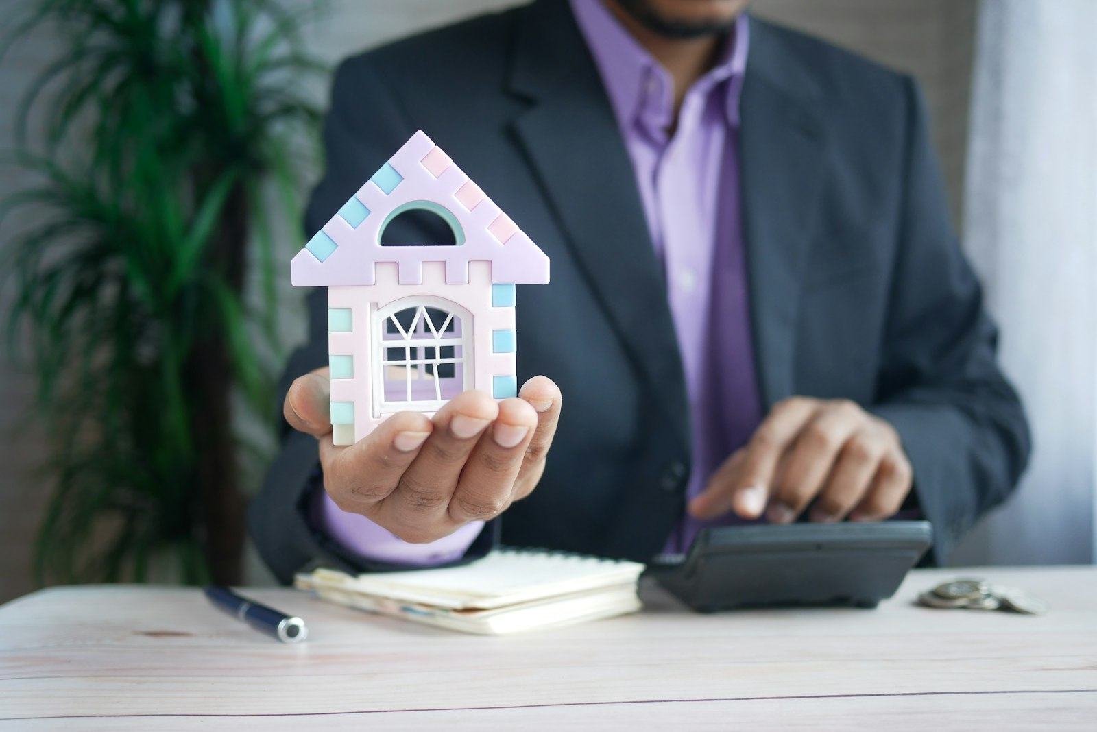 A man holding a model house next to a calculator